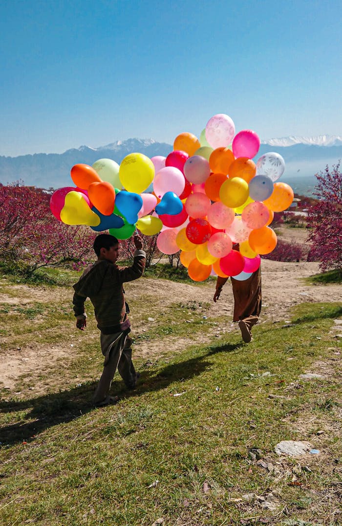 A child joyfully carries colorful balloons outdoors in Parwan, Afghanistan, with mountains in the background.