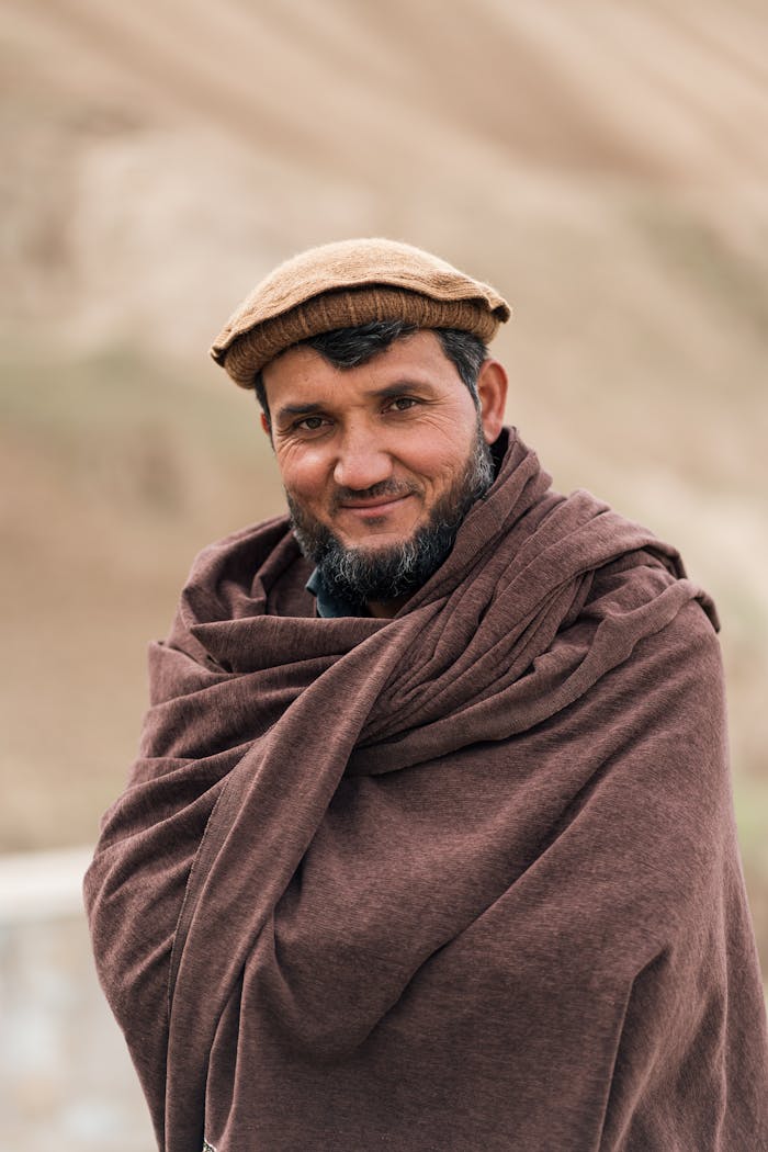 A smiling Afghan man in traditional attire outdoors, showcasing cultural heritage.