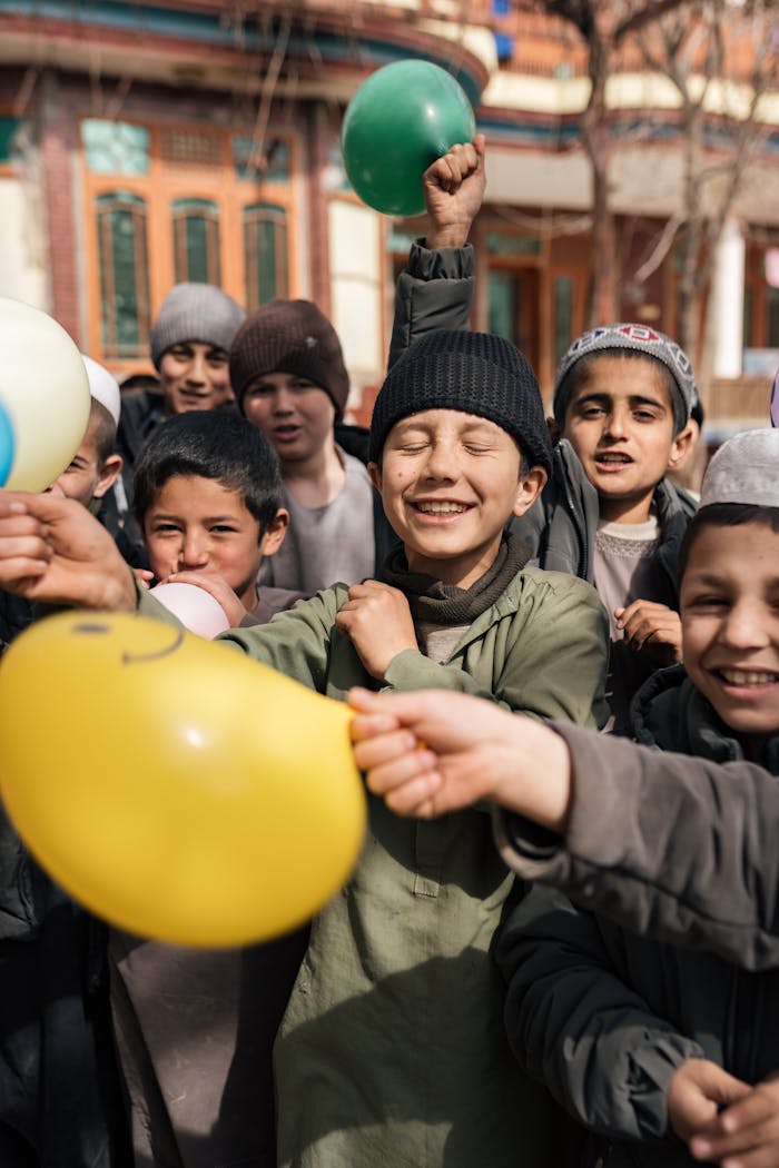 A group of Afghan children happily playing outdoors with colorful balloons, showcasing joy and unity.